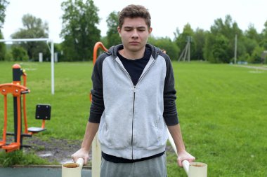 Ergen barlarda şınav çekiyor, temiz havada antrenman yapıyor, ön tarafa bakıyor.