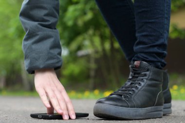 Kız sokakta akıllı bir telefon bulur ve onu asfalttan kaldırır. Yakın plan, yüzü yok.