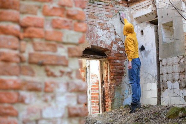 Young guy draws spray paint on the wall of an abandoned building, no face