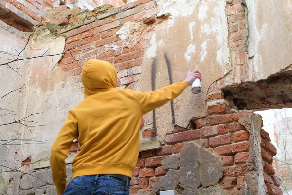 A young guy draws on the wall of an abandoned building. Teen uses spray paint in spray can.