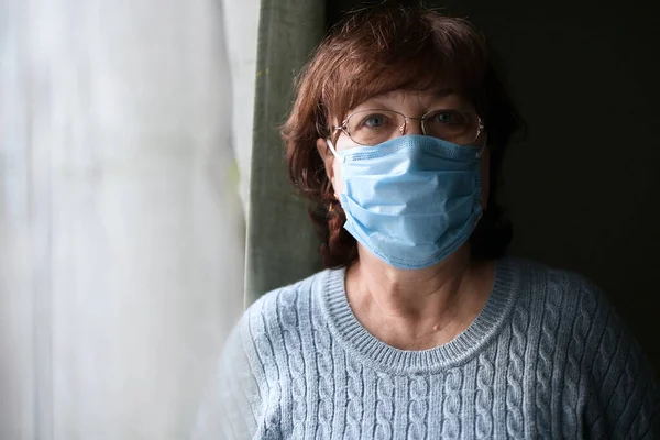 Mujer Anciana Con Una Máscara Médica Está Cerca Una Ventana —  Fotos de Stock