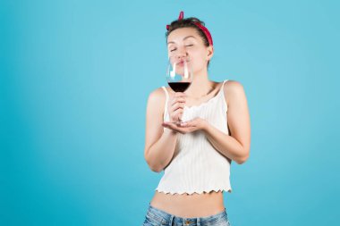 Tişörtlü ve bandanalı bir kız elinde büyük bir bardak şarap tutuyor ve aromasını içine çekiyor.