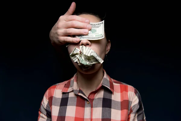 Crumpled dollars are in the woman s mouth, her eyes are closed by a stranger s hand and a hundred-dollar bill. Money made the woman close her eyes and be silent. Corruption, blackmail