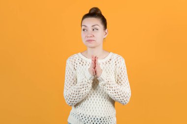 Genç kız ellerini ovuşturarak kurnazca bakışlarını kaçırıyor. Sarı arka planda izole edilmiş.