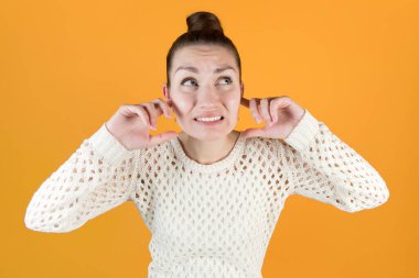 Genç kadın kulaklarını sıkıca kapatır ve öfkeyle yukarı bakar. Geniş açı, yakın çekim, turuncu-sarı izole edilmiş.