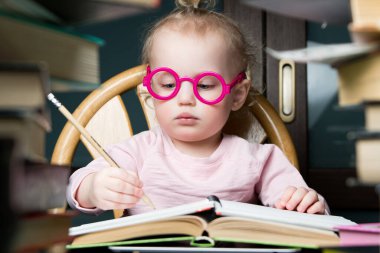 Oyuncak gözlüklü bir çocuk masadaki not defterine sanki yetişkin bir öğrenci not alıyormuş gibi çizer.