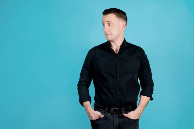 Siyah gömlekli genç bir adam usulca gülümseyip yüzünü çevirir. Mavi üzerine izole edilmiş.