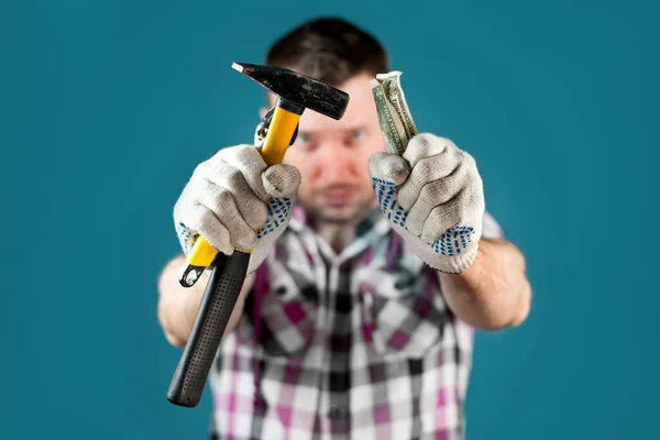 a hard worker in a crippled shirt holds out tools and crumpled dollars into the camera. Selective focus on hands in dirty gloves. Symbol of low manual hard labor