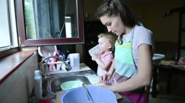 Küçük kızı yakınlarda oynarken genç bir kadın yemek yapmakla meşgul.