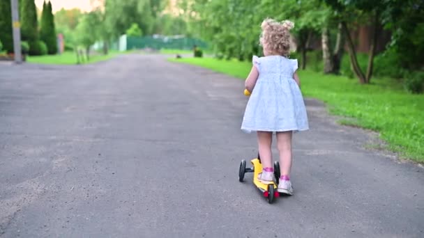 Küçük kız kamerayı çocuklar için bir scooterın üzerinde bırakıp arkasına bakıyor. — Stok video