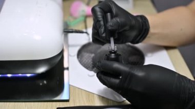 Siyah koruyucu eldivenlerin ustası fırçayı vernikle tüpe daldırıyor.