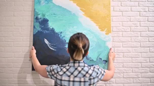Het meisje hangt een olieverfschilderij aan de muur en bewondert haar — Stockvideo