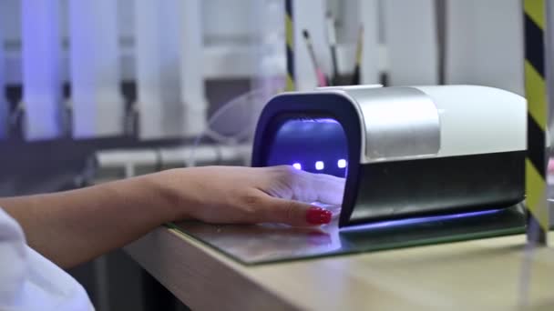 The girl s hand lies in an ultraviolet lamp to affect the coating of nails — Stock Video