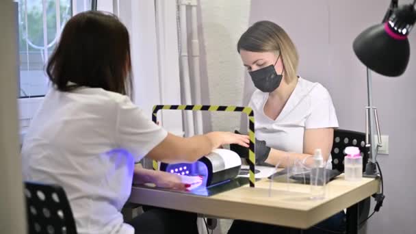 Mästaren i en skyddande mask och handskar serverar flickan i en skönhetssalong — Stockvideo