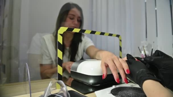 El cliente recibe un servicio en un salón de manicura a través de un cristal protector — Vídeo de stock