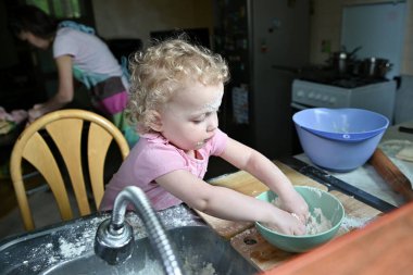 Annem yemek yapmakla meşgulken küçük bir kız mutfakta kabadayıdır. Çocuk mutfakta unla oynuyor.