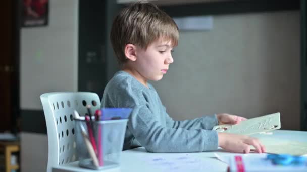 En gutt sitter ved et bord og skal til å lage håndverk av tredeler – stockvideo