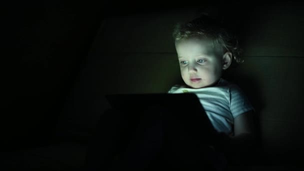Egy kislány rajzfilmeket néz egy táblán a sötétben. — Stock videók