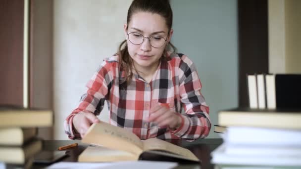 Chica se está preparando para los exámenes, buscando material en un libro, hojeando a través de ella — Vídeo de stock