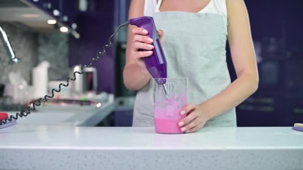 Woman whips pink icing for cake in bright kitchen. — Stock Video