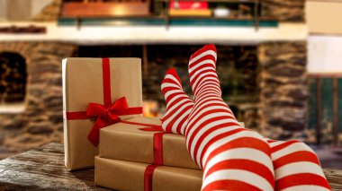 Kırmızı ve beyaz Noel çoraplı sıska genç kadın bacakları. Şömine arkaplanı ve kış zamanı. Dekorasyon ve Noel hediyeleriniz için boş yeriniz olan masa üstü. Ormanda kar taneleri ve don, uzayı kopyala.
