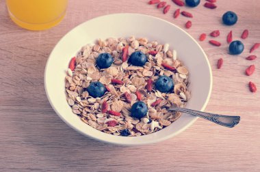 Müsli yulaf ezmesi ve mısır gevreği beyaz bir tabak, havadar pirinç, goji çilek ve yaban mersini ile. Bej ahşap arka plan.