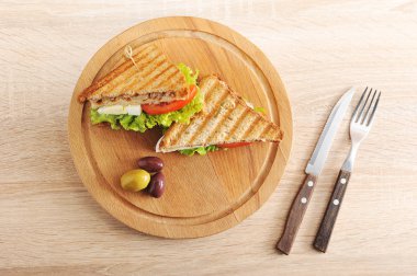 Tahta tepsiye ton balığı dolgusu yla kızarmış beyaz ekmekkulübü sandviçi. Sandviç ikiye bölünür. Yakınlarda birkaç zeytin var. Açık ahşap bir yüzey çatal üzerinde. Close. Yukarıdan görüntüle.