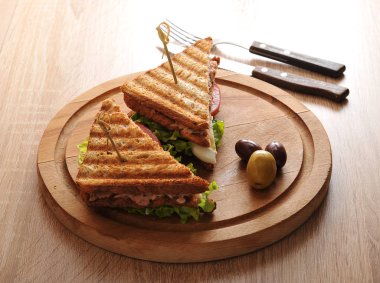 Beyaz tost ekmeğinden ton balığı ile sandviç. Ton balığı, yumurta, domates, yeşil salata. Sandviç tahta yuvarlak tepside. Yakınlarda birkaç zeytin var. Yukarıdan görüntüleyin. Makro fotoğrafçılık.