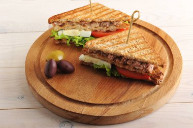 Tahta tepsiye ton balığı dolgusu yla kızarmış beyaz ekmekkulübü sandviçi. Sandviç ikiye bölünür. Yakınlarda birkaç zeytin var. Açık ahşap arka plan. Close.