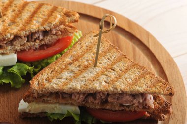 Beyaz tost ekmeğinden ton balığı ile sandviç. Ton balığı, yumurta, domates, yeşil salata. Sandviç tahta yuvarlak tepside. Yakınlarda birkaç zeytin var. Yukarıdan görüntüleyin. Close.