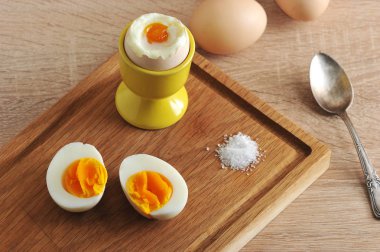 Tahta tepside, haşlanmış yumurta, tuz ve haşlanmış yumurtanın iki yarısı. Ahşap ışık arka plan. Close. 