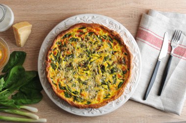 Beyaz bir tabak ta ıspanak ve yeşil soğan ile quiche Kek pasta. Sonraki Parmesan peyniri, yeşil soğan, ıspanak, kabuksuz çiğ yumurta ile kase. Peçete kumaş ve çatal bıçak takımı yapılmış. Yukarıdan görüntüle.
