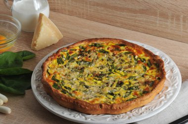 Beyaz bir tabak ta ıspanak ve taze soğan ile quiche açık pasta. Kremalı cam sürahiyanında, Parmesan peyniri, yeşil soğan, ıspanak yeşilliği, kabuksuz çiğ yumurtalı cam kase.