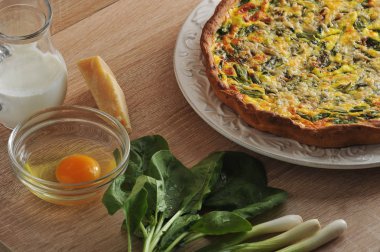 Beyaz bir tabak ta ıspanak ve taze soğan ile quiche açık pasta. Kremalı cam sürahiyanında, Parmesan peyniri, yeşil soğan, ıspanak yeşilliği, kabuksuz çiğ yumurtalı cam kase.