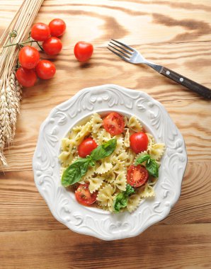 Pesto soslu makarna farfalle ve çeri domates. Makarna taze fesleğen yaprakları ile dekore edilmiştir. Arka planda, buğday kulakları ve domates. Dikey yönlendirme. Yukarıdan görüntüleyin. Closeup.