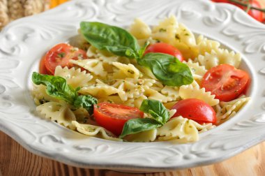 Pesto soslu makarna ve derin beyaz bir tabakta çeri domates. Makarna taze fesleğen yaprakları ile dekore edilmiştir. Açık ahşap arka plan. Close. Makro fotoğrafçılık.
