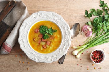 Bir tabakta füme et li bezelye çorbası. Kumaş peçete. Tabağın yanında, bir kaşık ve baharatlar: sarımsak, maydanoz, yeşil soğan ve biber. Açık ahşap arka plan. Yukarıdan görüntüle.