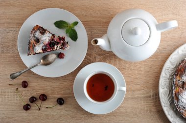 Çanak bir kiraz ile bir lor-çikolata lı brownie üzerinde. Tabakta kek parçası. Bir fincan çay ve çaydanlık. Taze kirazlar masada. Yukarıdan görüntüleyin. Close.