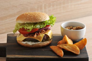 Iştah açıcı çizburger ve patates ahşap bir tahta üzerinde rustik vardır. Çizburger dolgusunda, Çedar peyniri ve kızarmış pastırma. Sırada bir bardak hardal çatal bıçak takımı var. Close.