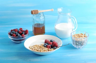 Sağlıklı bir kahvaltı servis: müsli, ahududu ve yaban mersini, bal, cam sürahi yoğurt. Mavi ahşap arka plan. Close.