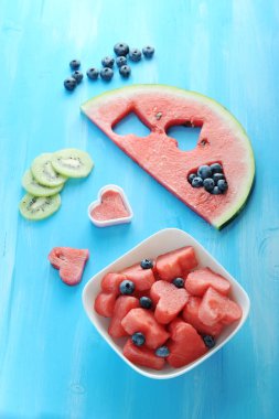 Mavi bir arka plan, yaban mersini, kivi dilimleri, bir dilim karpuz. Sonra karpuz hamuru ile bir tabak, bir kalp şeklinde kesilmiş. Yukarıdan görüntüleyin. Çerçevenin dikey yönü.