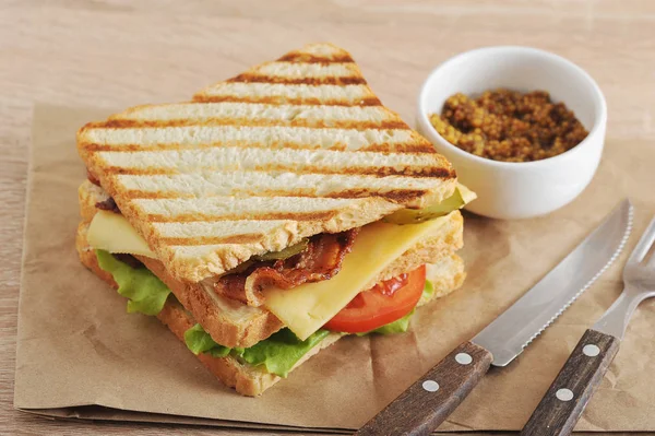 Tavuk göğsü, pastırma, yeşil salata, peynir, domates ve salatalık turşusu dolu bir klasik kulüp sandviç. Bir sonraki çatal bıçak takımı ve bir fincan hardal. Close.