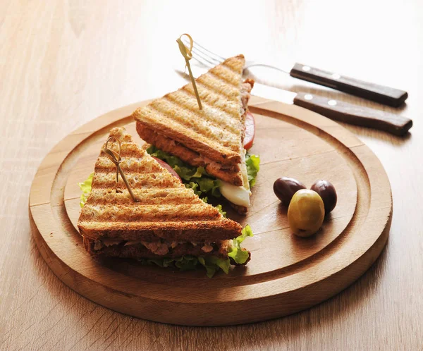 Tahta tepside ton balığı dolu kızarmış beyaz ekmekbir sandviç. Yakınlarda çatal bıçak takımı var. Açık ahşap arka plan. Close.