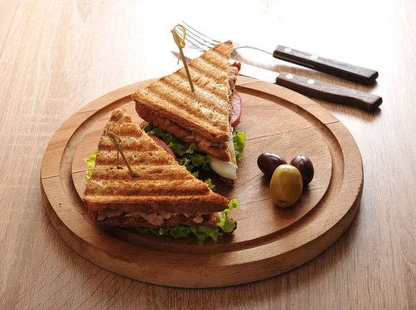 Beyaz tost ekmeğinden ton balığı ile sandviç. Ton balığı, yumurta, domates, yeşil salata. Sandviç tahta yuvarlak tepside. Yakınlarda birkaç zeytin var. Yukarıdan görüntüleyin. Makro fotoğrafçılık.