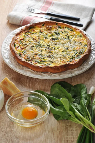 Beyaz bir tabak üzerinde ıspanak ve yeşil soğan ile quiche açık pasta. Sonraki Parmesan peyniri, yeşil soğan, ıspanak yeşillikleri, kabuksuz çiğ yumurta ile cam kase. Peçete kumaş ve çatal bıçak takımı yapılmış.