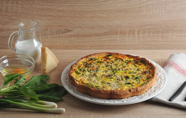 Bir tabakta ıspanak ve taze soğan ile quiche açık pasta. Krema, Parmesan peyniri, yeşil soğan, ıspanak yeşillikleri, çiğ yumurta ile cam kase ile sürahi yanında. Peçete kumaş ve çatal bıçak takımı yapılmış.