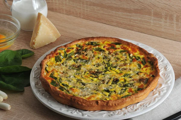 Beyaz bir tabak ta ıspanak ve taze soğan ile quiche açık pasta. Kremalı cam sürahiyanında, Parmesan peyniri, yeşil soğan, ıspanak yeşilliği, kabuksuz çiğ yumurtalı cam kase.