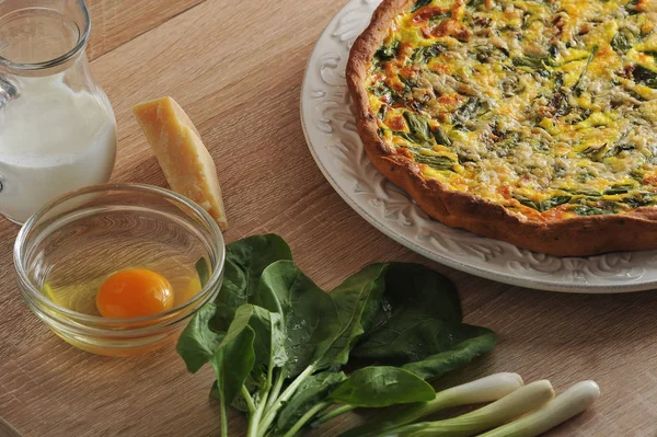 Beyaz bir tabak ta ıspanak ve taze soğan ile quiche açık pasta. Kremalı cam sürahiyanında, Parmesan peyniri, yeşil soğan, ıspanak yeşilliği, kabuksuz çiğ yumurtalı cam kase.