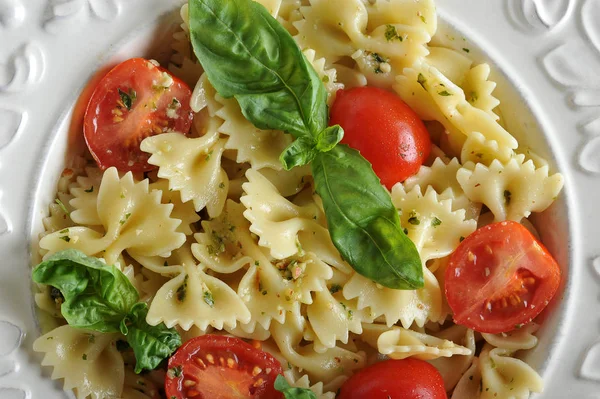 Pesto soslu makarna farfalle ve derin beyaz bir tabakta kiraz domates. Makarna taze fesleğen yaprakları ile dekore edilmiştir. Açık ahşap arka plan. Yukarıdan görüntüleyin. Close. Makro fotoğrafçılık.