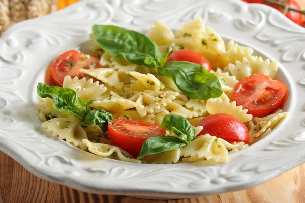 Pesto soslu makarna ve derin beyaz bir tabakta çeri domates. Makarna taze fesleğen yaprakları ile dekore edilmiştir. Açık ahşap arka plan. Close. Makro fotoğrafçılık.